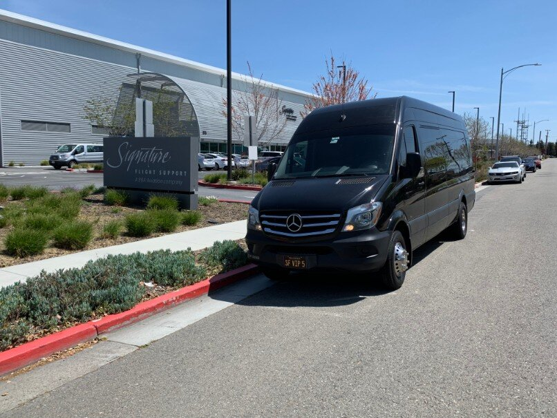 Black Mercedes Sprinter van parked outside the Signature Flight Support private aviation terminal on a clear day.