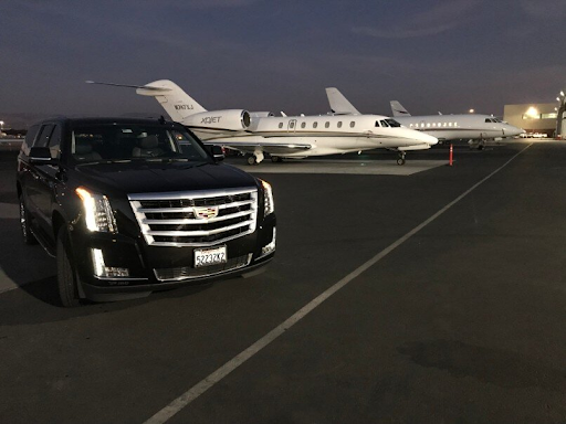 Black Cadillac Escalade parked on an airport tarmac at dusk with a private jet in the background.