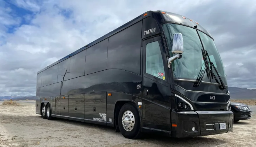 Black MCI motorcoach parked on a gravel lot under cloudy skies