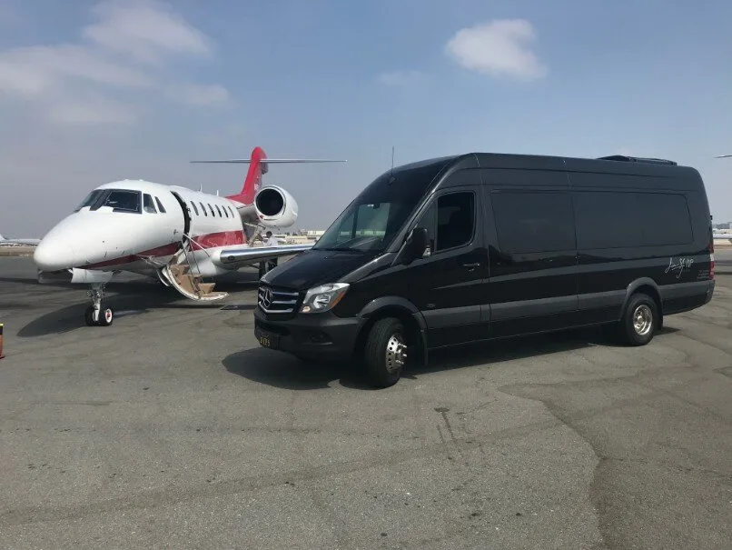 Black Mercedes-Benz Sprinter van beside a private jet