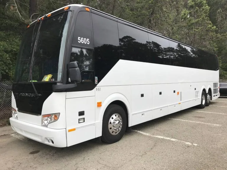 White Prevost motorcoach parked in a lot surrounded by trees