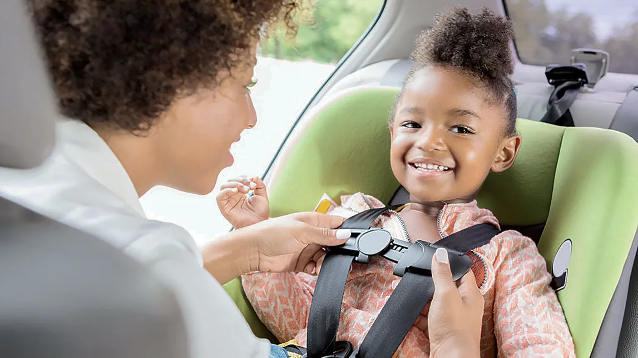 Adult buckling a smiling child into a car seat