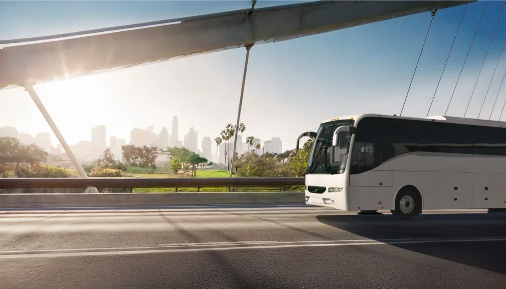 White motorcoach driving across a highway bridge toward a city skyline