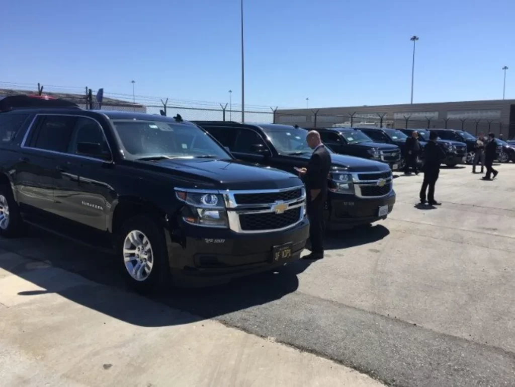 Row of black Chevrolet Suburbans lined up at an airport curb
