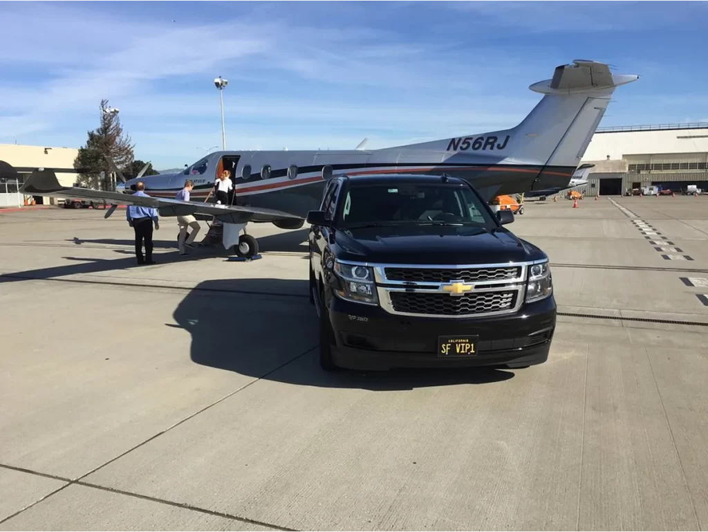 Black Chevrolet Suburban on an airport tarmac beside a private turboprop plane