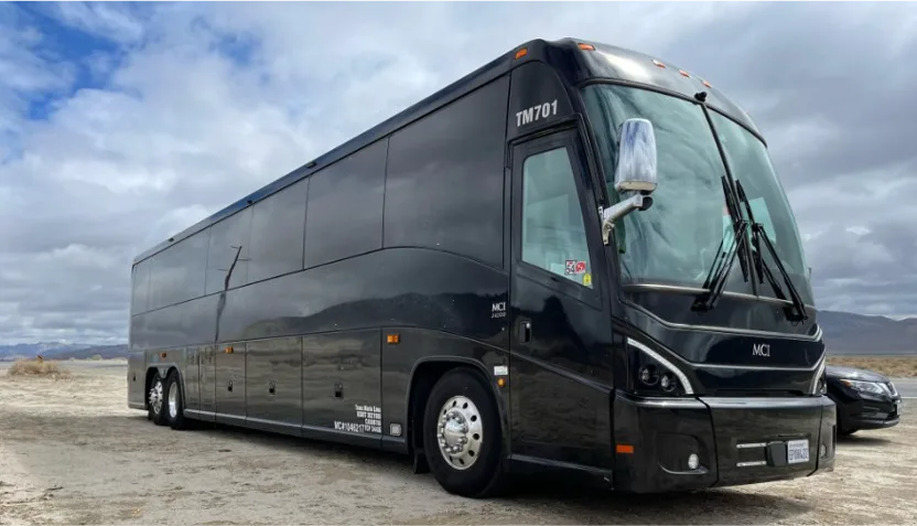 Black MCI motorcoach parked under a cloudy sky