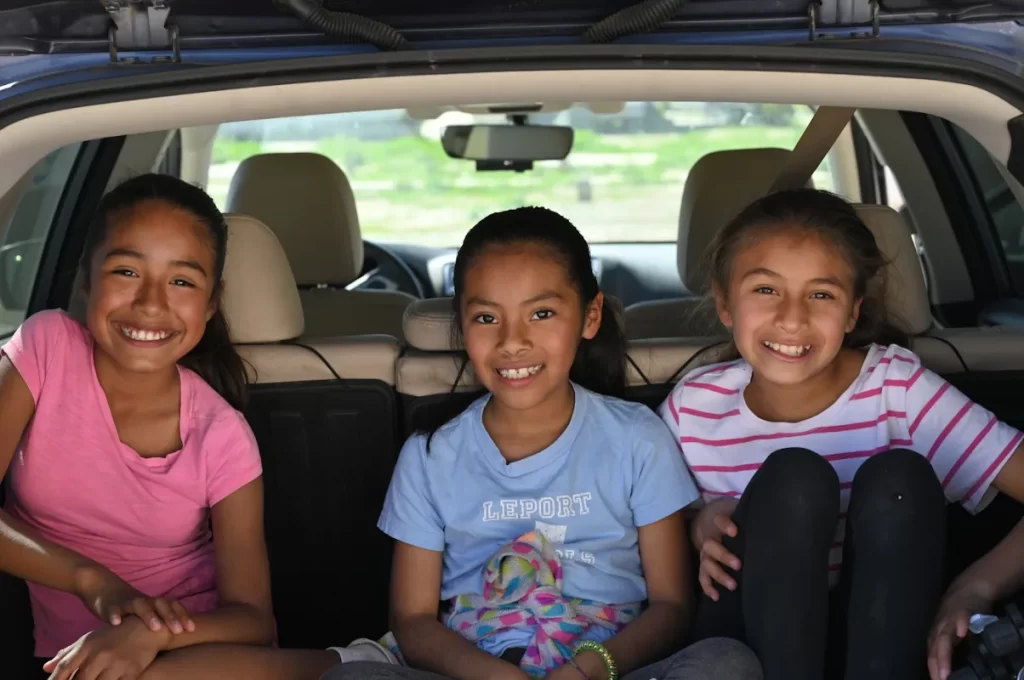 Three smiling girls sitting in the back of an SUV
