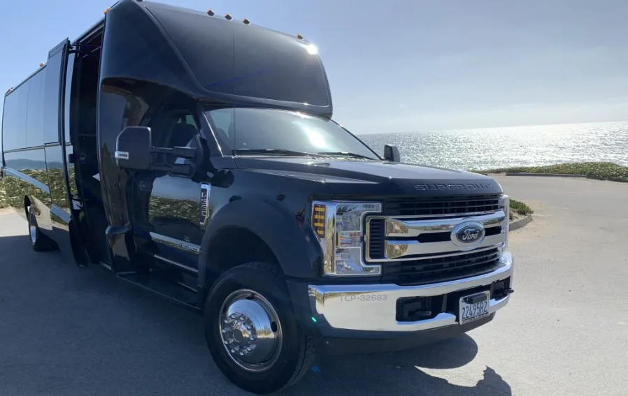 Black Ford mini coach with its door open beside the ocean