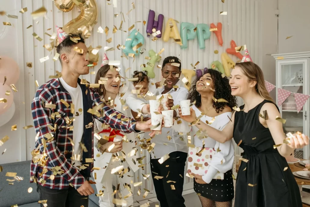 Friends toasting at a birthday party with falling confetti and balloons