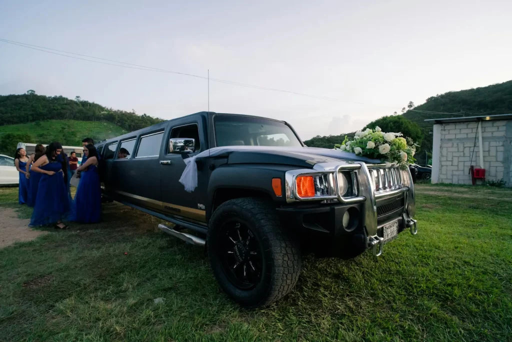 Black Hummer stretch limo on grass with prom guests in gowns behind it