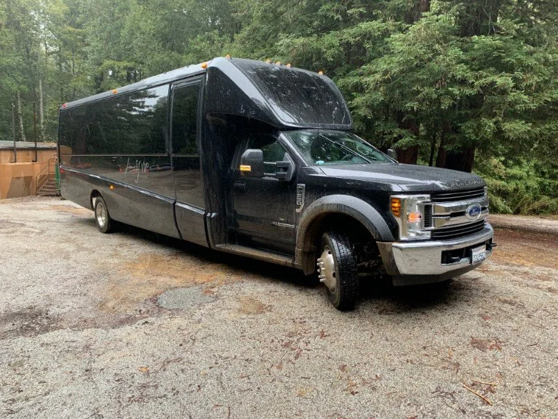 Black Ford shuttle bus parked on a forest gravel road